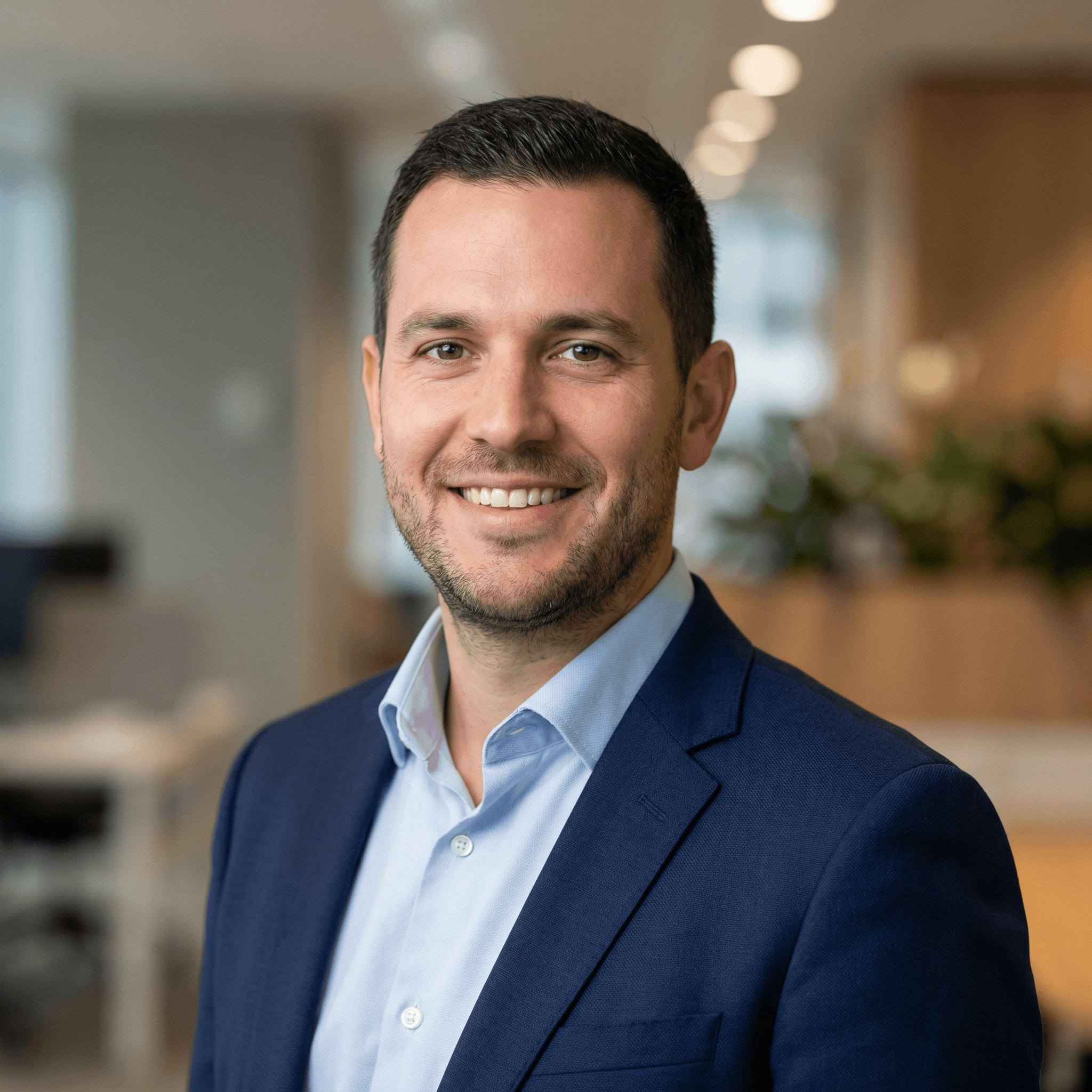 Foto de perfil LinkedIn masculina gerada por IA — homem sorrindo com paletó azul marinho e camisa social, escritório moderno ao fundo